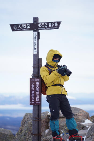 冬の山頂でカメラを触る登山者