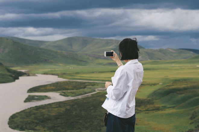 山岳風景にスマホのカメラを向ける女性